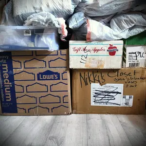 A photograph of the boxes mentioned in the blog post. From left to right: a Lowe's box with "medium" on the left side; to the right of it a box with red script that says, "Gift Box Apples"; below that one a box with handwriting that says, "Nikki's Closet".  The boxes sit on gray vinyl flooring. They are topped with one smaller plastic box and many plastic bags.
