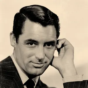 A publicity headshot of Cary Grant in shades of black, grey, and yellow. Grant in looking at the viewer with piercing dark eyes and a slight smile. His left had is near is left ear giving the image a casual feel, but his suit says he is all business.