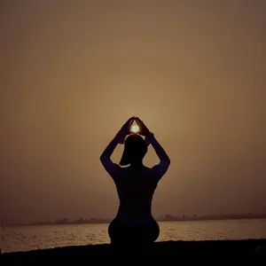 A woman silhouetted against the light of a low hanging moon. Her arms are raised above her head, and she appears to be holding the moon in her hands. The color palette is of warm browns.