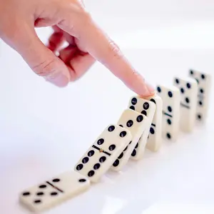 A hand is coming in from above touching a row of dominoes and beginning the chain reaction. The background is white, and the dominoes are white with black dots.