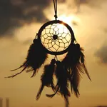 An image of a dreamcatcher moving in the breeze and silhouetted by a dramatic orange sky.