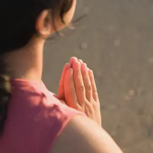 An image taken over the shoulder of a woman with her hands together holding sacred space. Only her hands are in sharp focus.