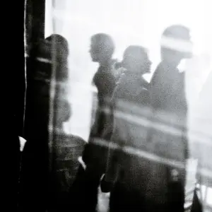 A somewhat abstract black and white image of people walking past a window. It is a study of dark and light.