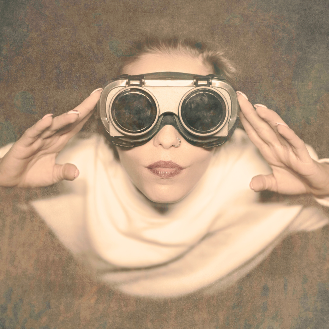 A vintage looking photograph of a woman. The perspective is from overhead looking down at her. She is looking up into a bright light and wearing big round goggles with big black lenses. Her hands are near here goggles, and she is focusing on what she is seeing. It's almost as if she is seeing into the future.