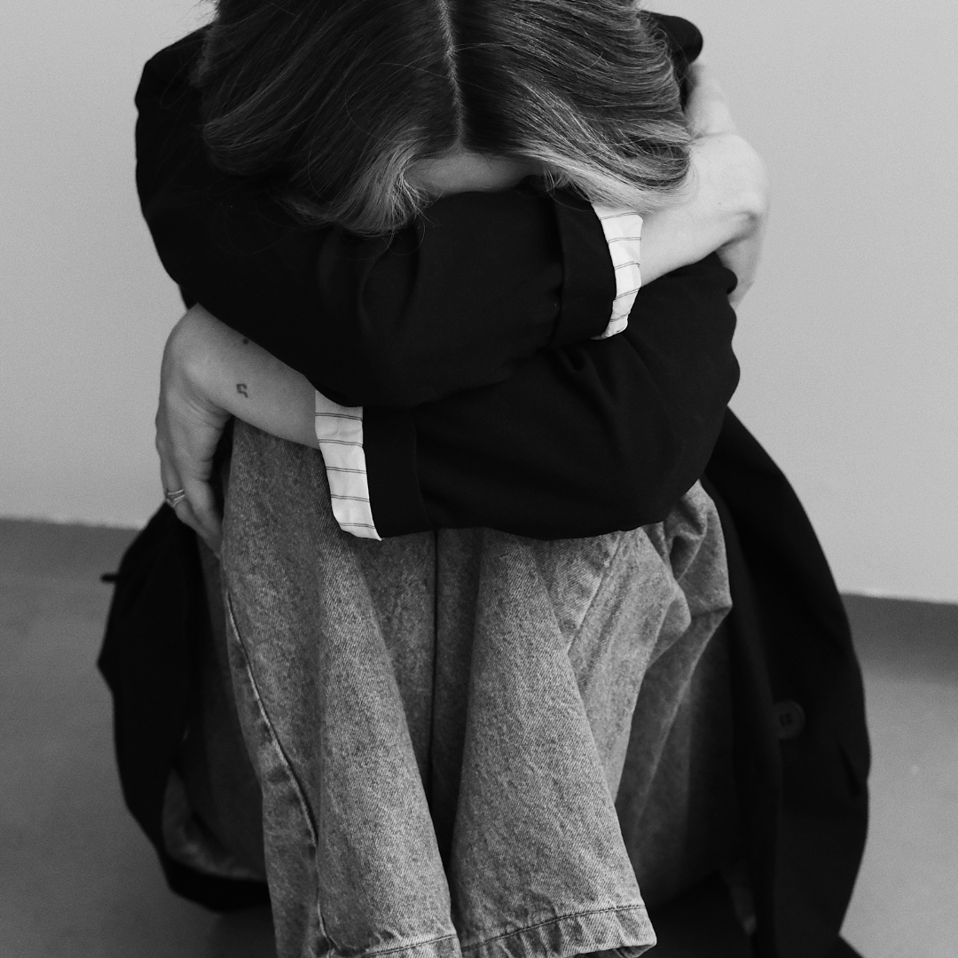 A black and white image of a woman curled up and holding herself in despair.
