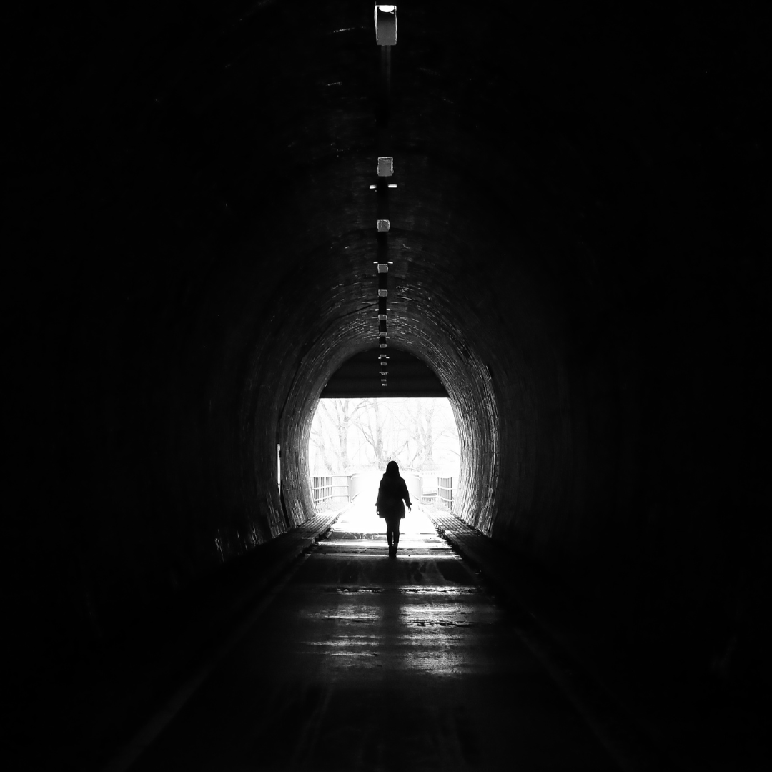 A person walking through a dark tunnel towards the light at the end of the tunnel. A person walking through a dark tunnel towards the light at the end of the tunnel.
