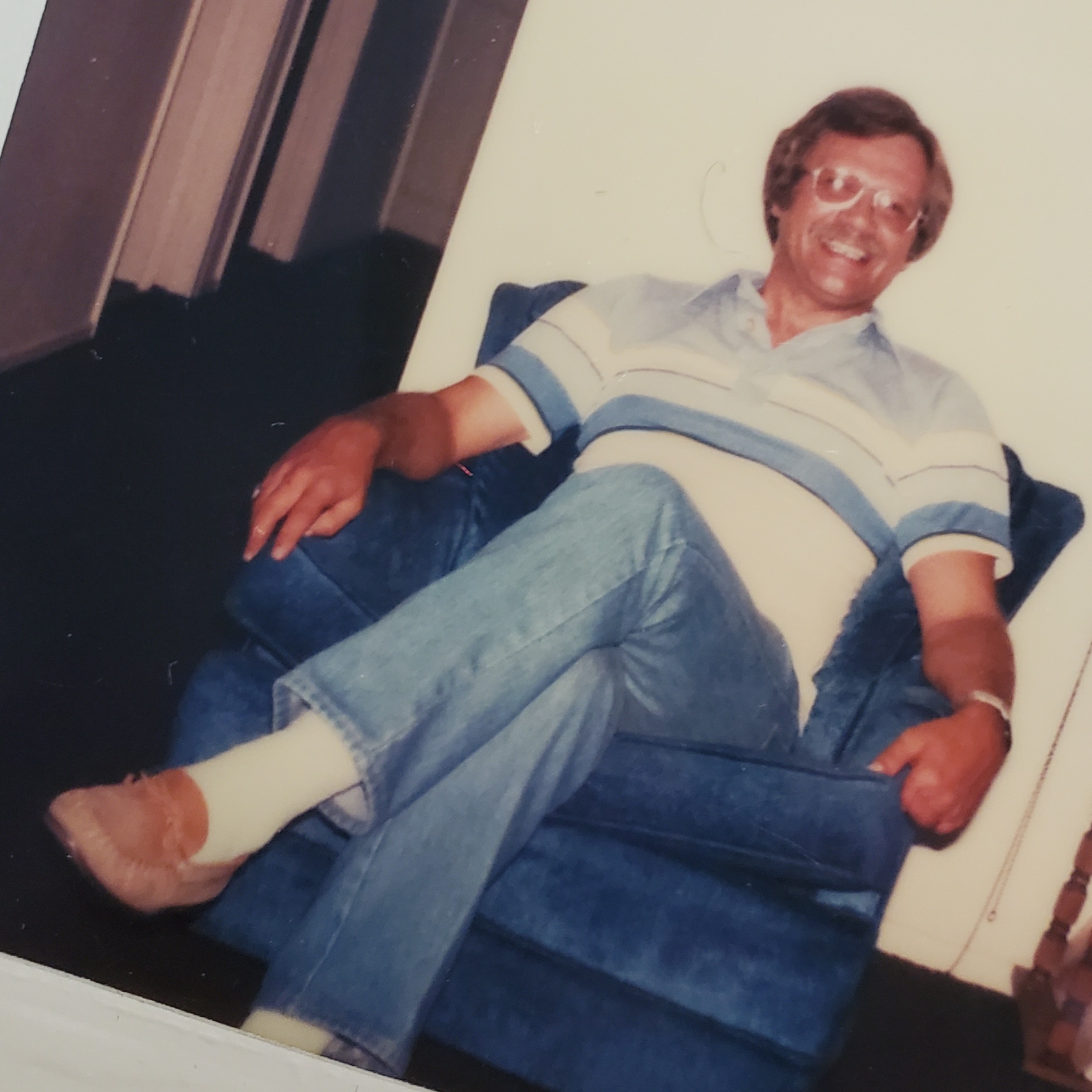 An old photograph of my dad, from the 1970's. He is sitting in a chair-tan and smiling.