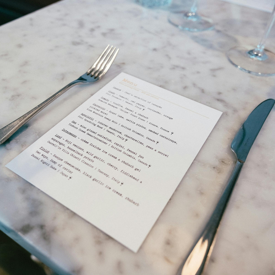 A photograph of a menu, knife, and fork on a marble table.