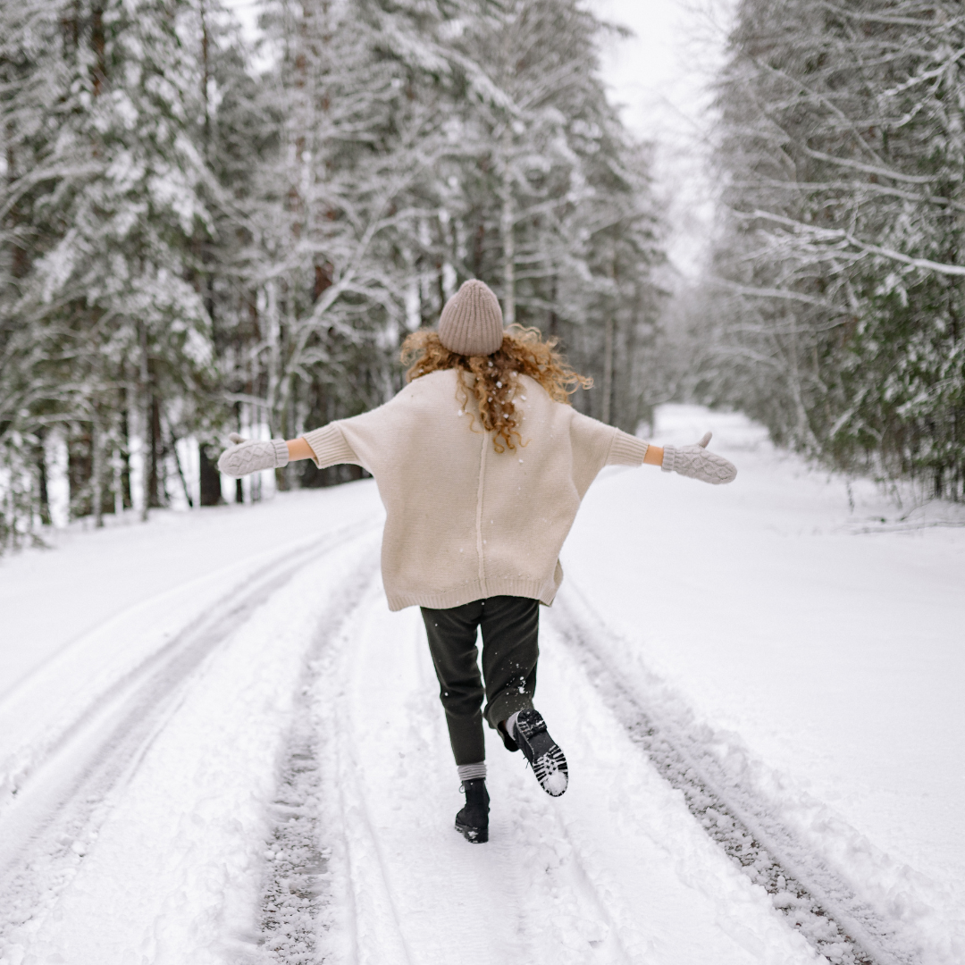 The image is of a woman walking joyfully down a snowy road. The image is of a woman walking joyfully down a snowy road.