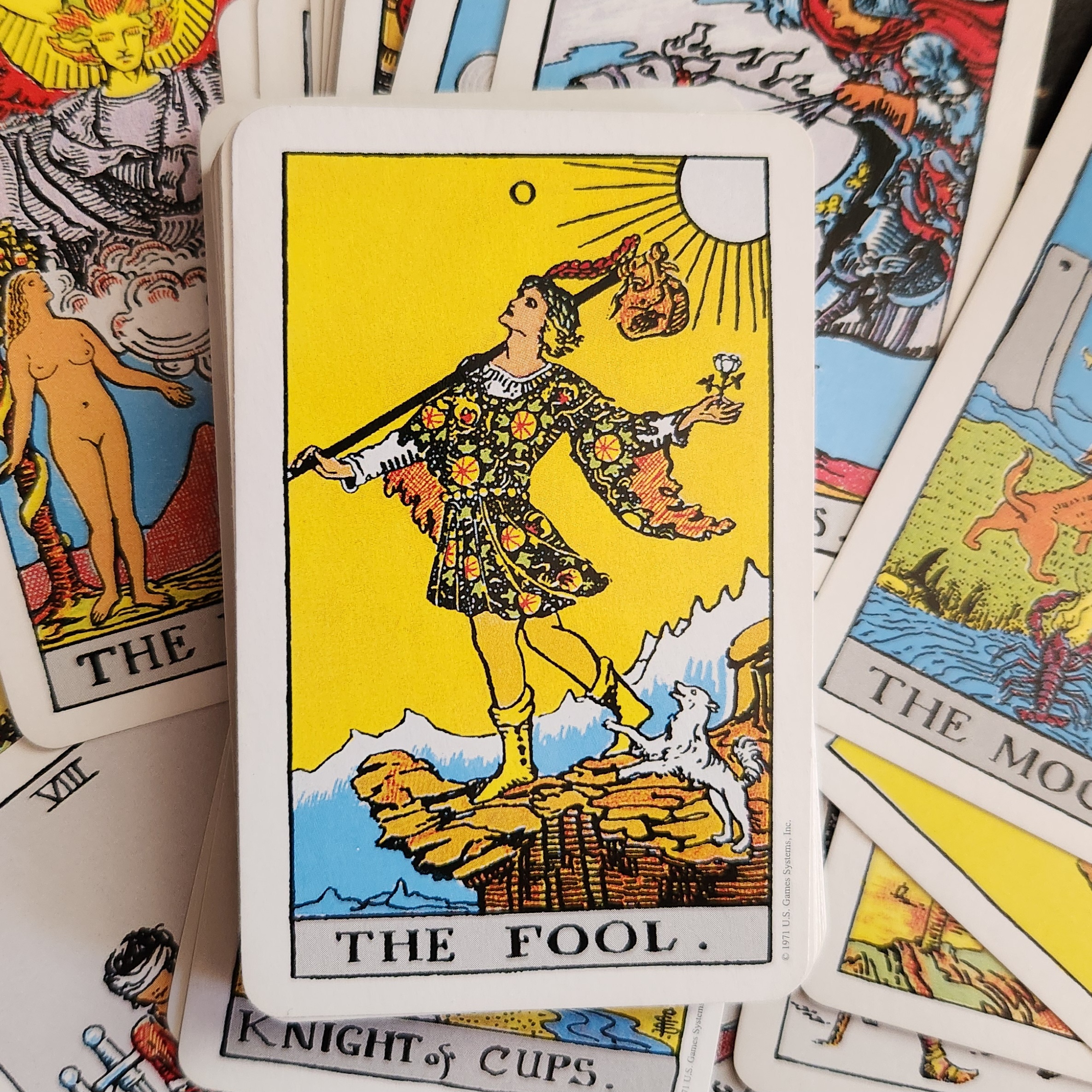 A photographic image of The Fool, card zero, from the Rider-Waite-Smith tarot deck. The background is the other cards scattered around.
