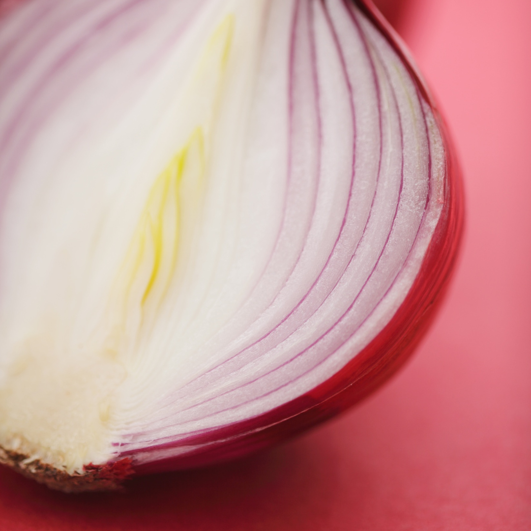 A close-up and partial image of a red onion highlighting the many layers. The background is a coral pink.