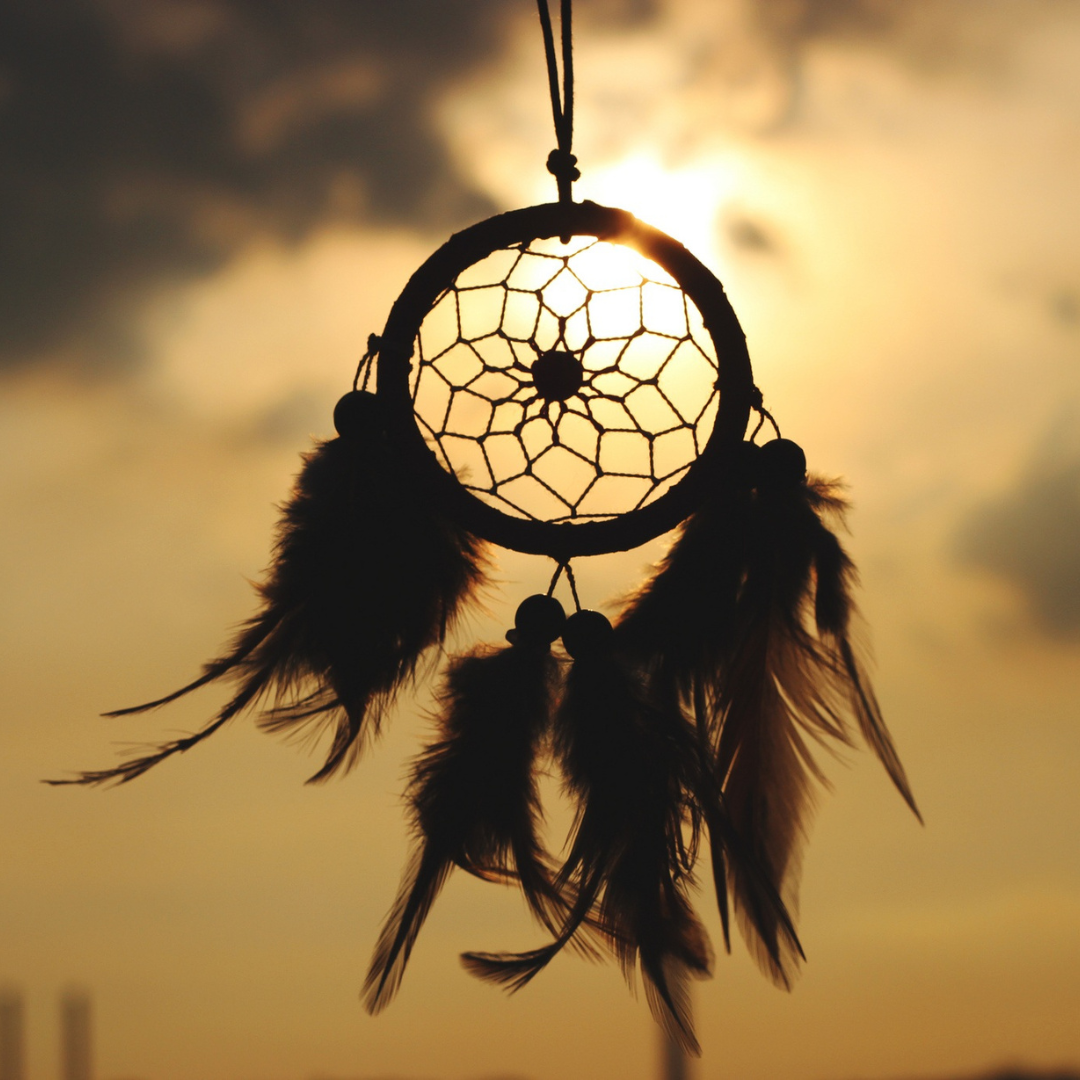 An image of a dreamcatcher moving in the breeze and silhouetted by a dramatic orange sky. An image of a dreamcatcher moving in the breeze and silhouetted by a dramatic orange sky.