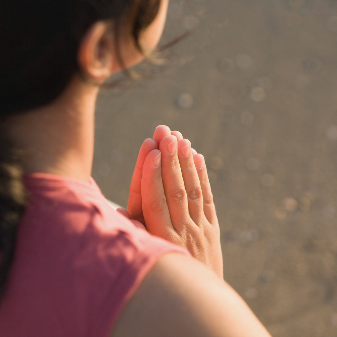 An image taken over the shoulder of a woman with her hands together holding sacred space. Only her hands are in sharp focus.